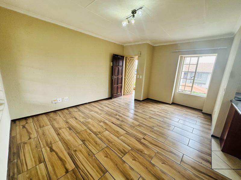 An empty living room featuring wood-look tile flooring, a security gate, and natural light from a casement window.