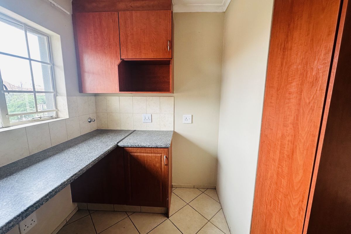 A compact kitchen area featuring wood-finish cabinetry, granite countertops, tiled backsplash, and ceramic floor tiles, offering a functional and clean workspace.