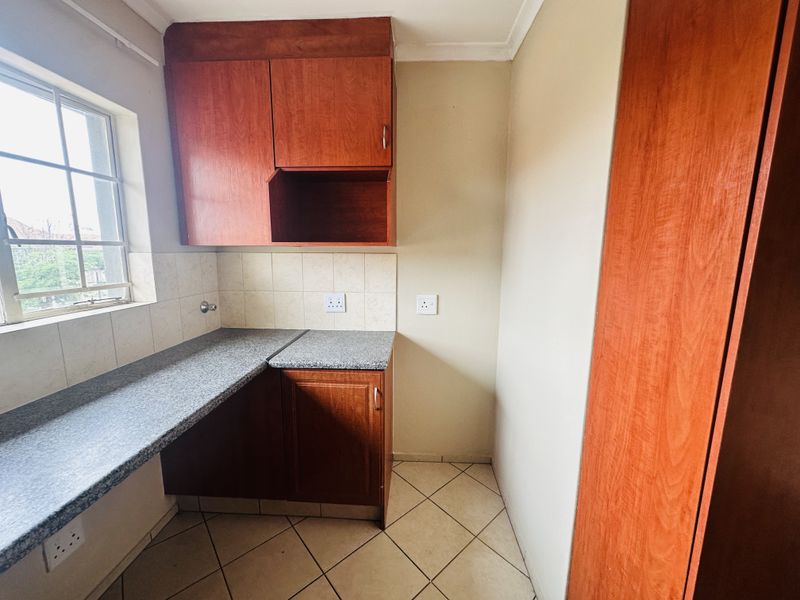 A compact kitchen area featuring wood-finish cabinetry, granite countertops, tiled backsplash, and ceramic floor tiles, offering a functional and clean workspace.