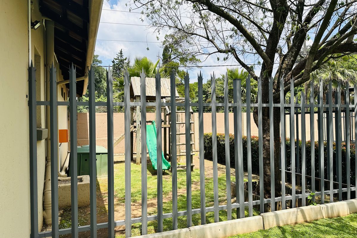 A view of the rear garden area featuring secure steel palisade fencing, a concrete curb, and established trees.