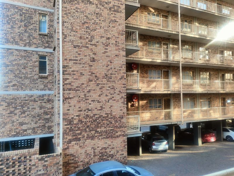 Exterior view of a multi-story face brick apartment building featuring private balconies and a ground-level covered parking area.
