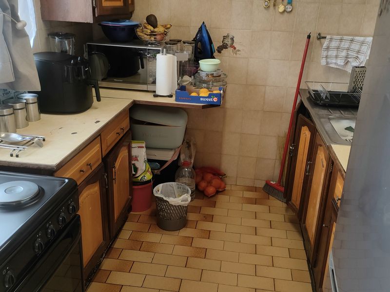 A compact kitchen featuring wooden cabinetry, tiled flooring, and a tiled backsplash, offering a functional layout with potential for modernization.