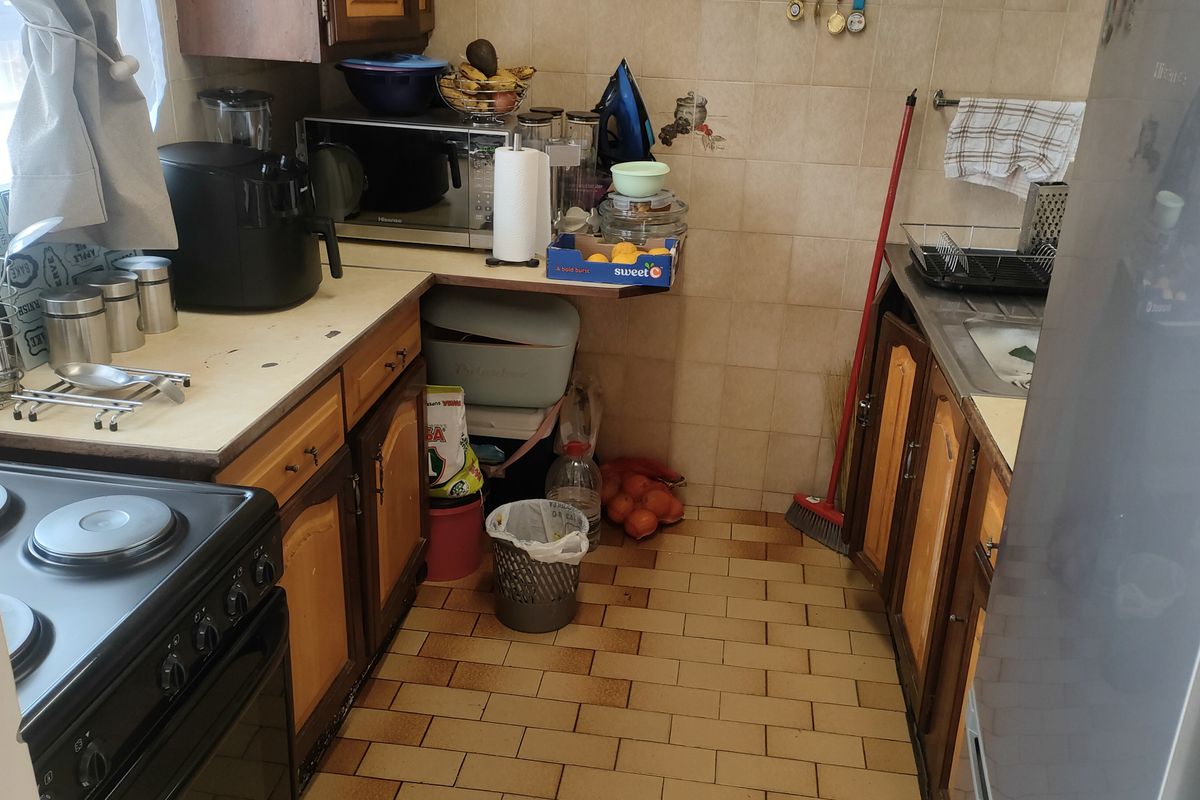 A compact kitchen featuring wooden cabinetry, tiled flooring, and a tiled backsplash, offering a functional layout with potential for modernization.