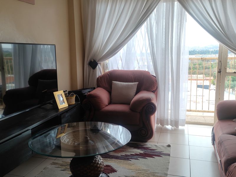 A living room featuring tiled flooring and a sliding glass door leading to a balcony with a security gate.