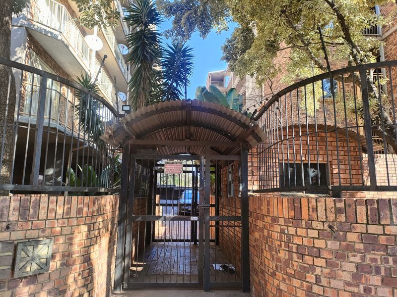 A secure pedestrian entrance featuring a brick boundary wall, wrought iron fencing, and a covered metal gate providing access to the apartment complex.