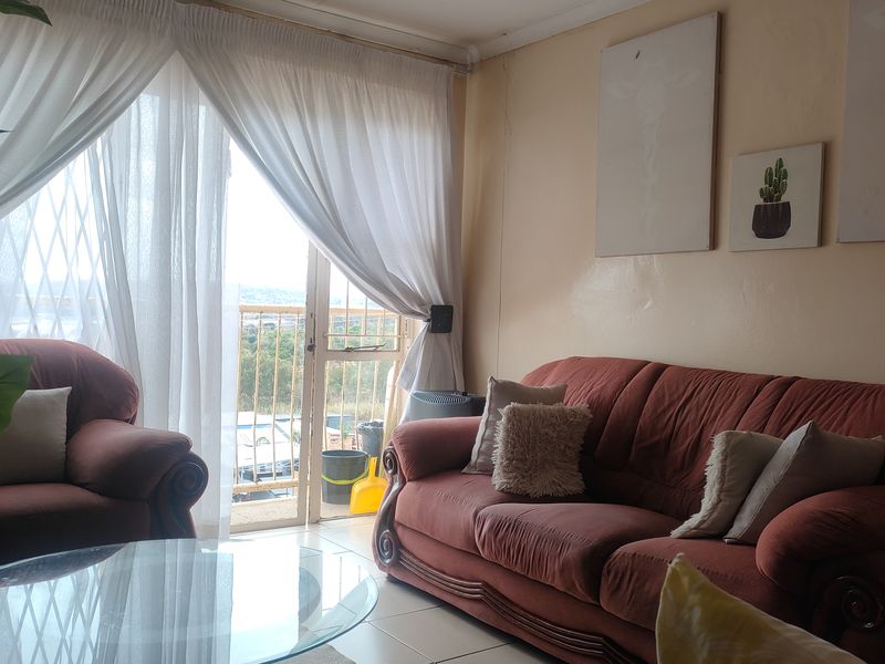 A living room featuring tiled flooring and a sliding glass door with a security gate, providing access to an outdoor balcony area.