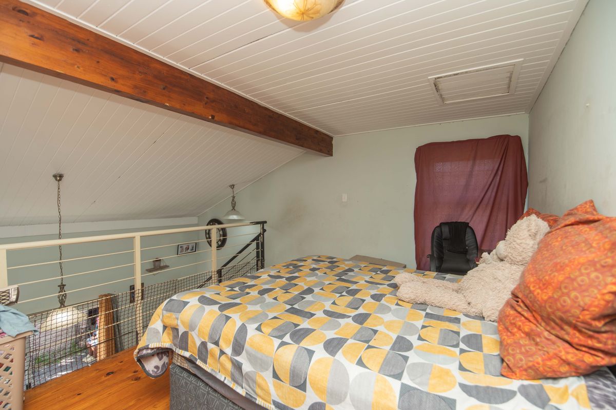 A loft-style bedroom featuring timber ceiling, exposed beam, and timber flooring, overlooking the lower level via a metal balustrade.