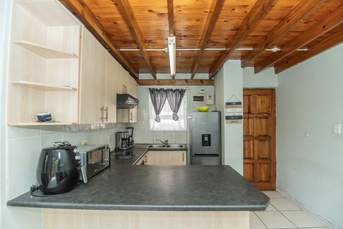 Functional kitchen featuring laminate cabinetry, dark countertops, stainless steel sink, extractor fan, and a distinctive exposed timber beam ceiling.