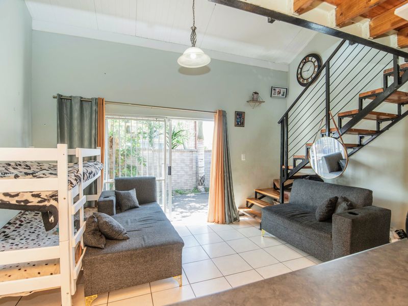 Open-plan living area featuring tiled floors, exposed timber ceiling beams, and a staircase leading to an upper level, with direct access to a patio.