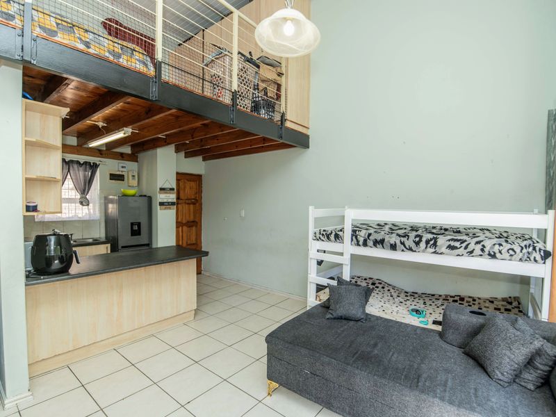 Open plan living area featuring a kitchen with built-in cabinetry and a mezzanine level with timber beams and metal safety railing.