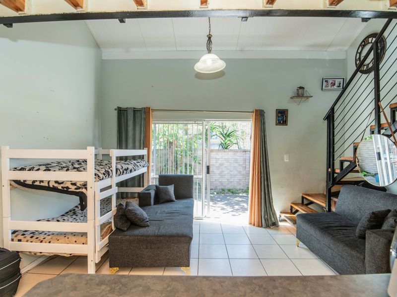 Open-plan living area featuring tiled floors, exposed ceiling beams, and a metal staircase, with direct access to an outdoor patio through sliding glass doors.