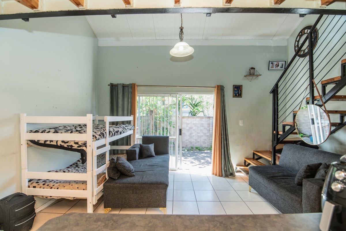 Open-plan living area featuring tiled floors, exposed ceiling beams, and a metal staircase, with direct access to an outdoor patio through sliding glass doors.