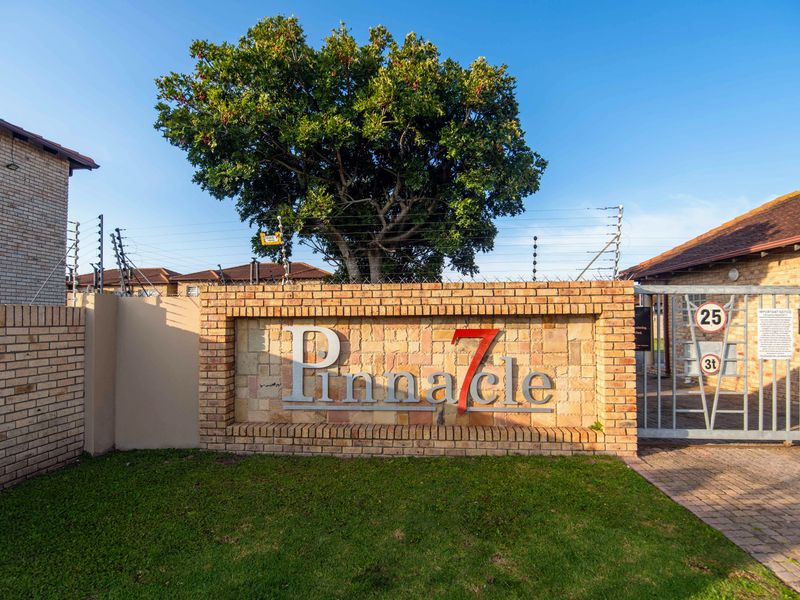 The entrance to Pinnacle 7 complex featuring a brick boundary wall, electric fencing, and a secure metal gate.