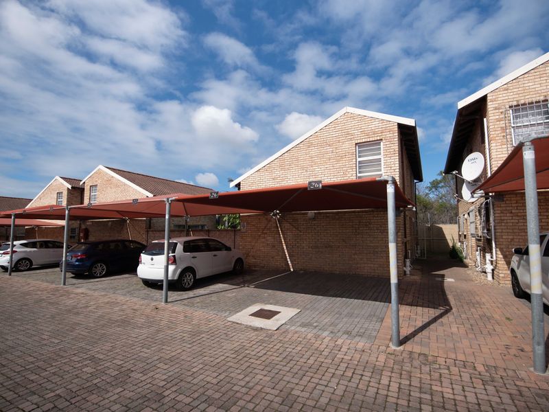 Exterior view of a townhouse complex featuring brick facades, paved driveway parking, and dedicated shade cloth carports for residents.