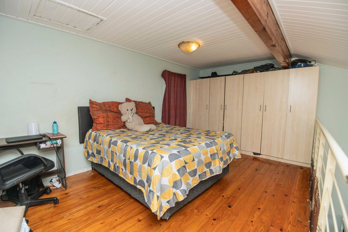 A loft-style bedroom featuring timber flooring, exposed ceiling beams, and extensive built-in wardrobe storage.