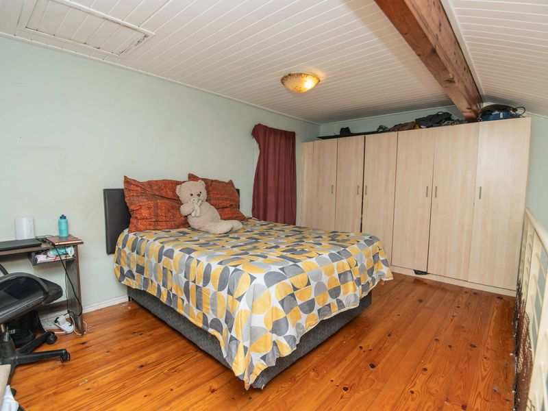A loft-style bedroom featuring timber flooring, exposed ceiling beams, and extensive built-in wardrobe storage.