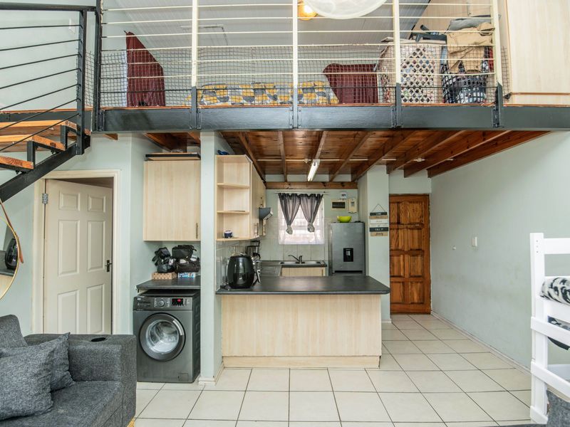 Open-plan living area featuring a mezzanine level, metal staircase, and a functional kitchen with tiled flooring and exposed timber ceiling beams.