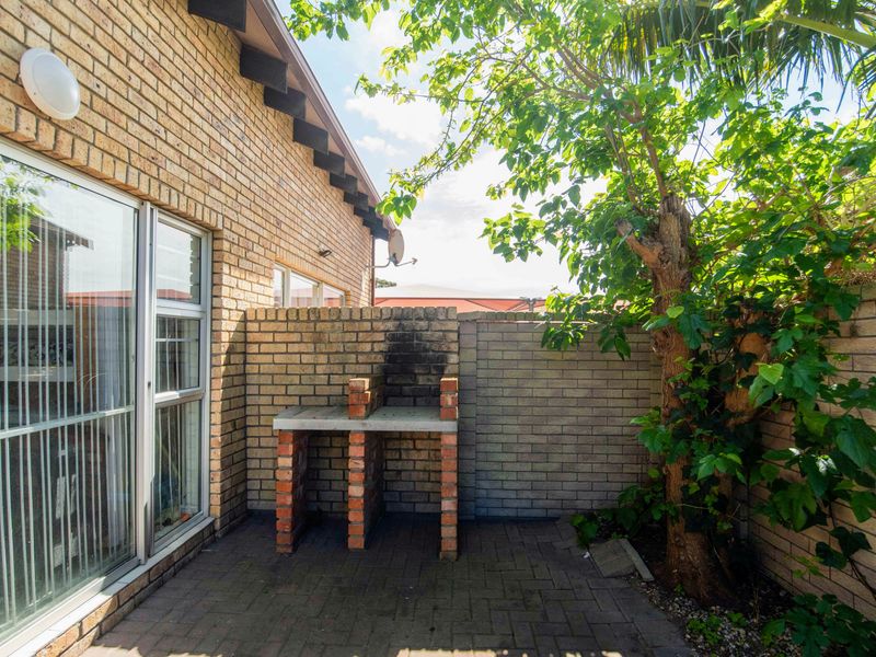 Private paved patio area featuring a built-in brick braai, enclosed by brick boundary walls and accessible via a sliding glass door.