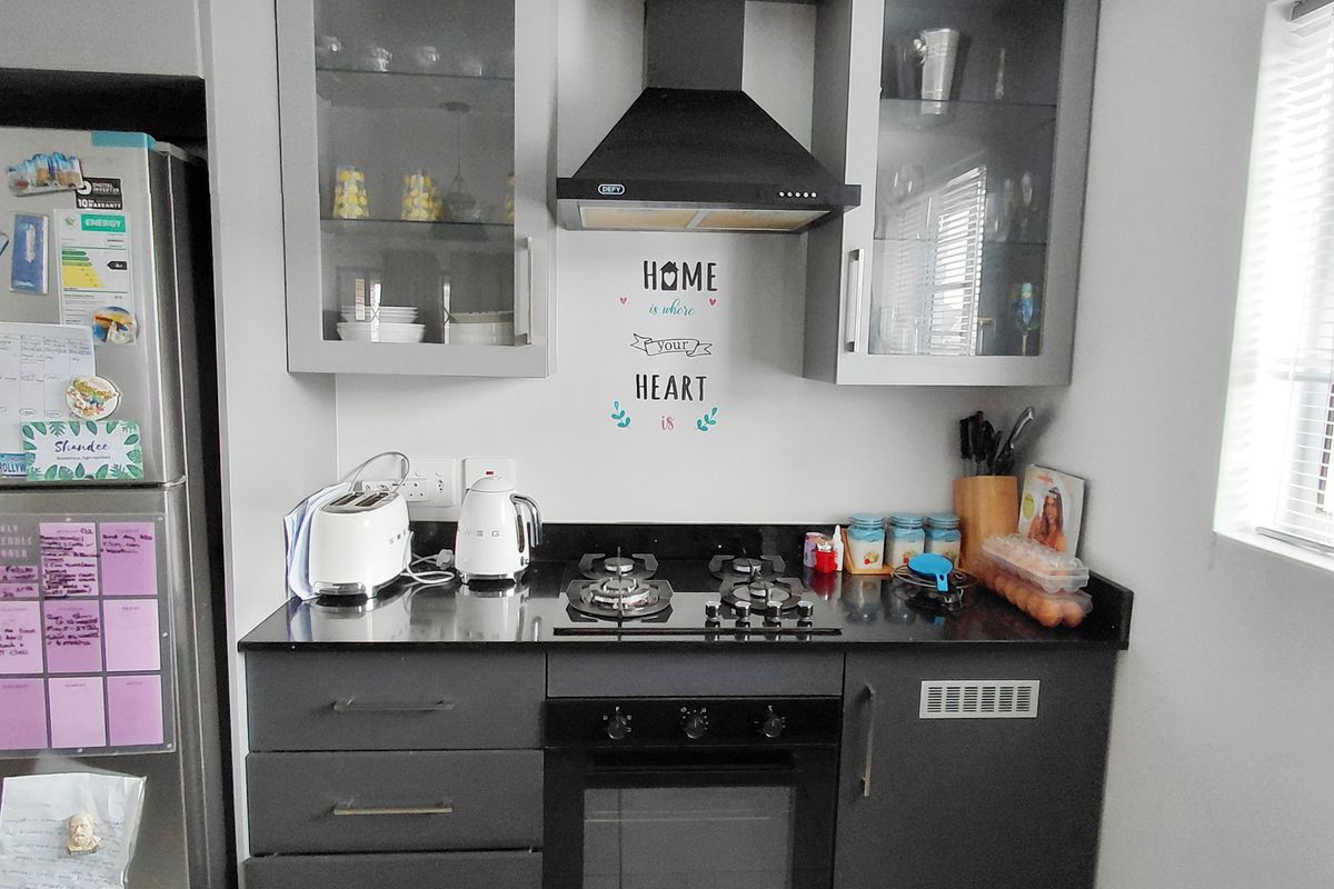 A compact, modern kitchen featuring dark cabinetry, granite countertops, a gas hob, built-in oven, and an extractor fan.
