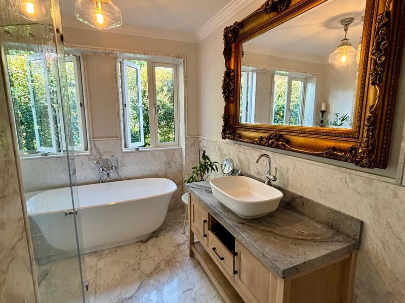 Luxurious bathroom featuring marble flooring and wall tiling, a freestanding bathtub, a stone-topped vanity with a vessel sink, and a glass-enclosed shower.
