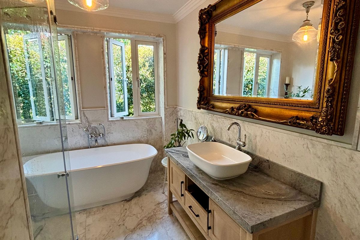 Luxurious bathroom featuring marble flooring and wall tiling, a freestanding bathtub, a stone-topped vanity with a vessel sink, and a glass-enclosed shower.