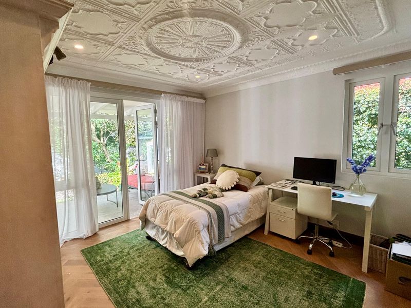 A well-lit bedroom featuring an ornate plaster ceiling, herringbone timber flooring, and sliding glass doors providing direct access to the outdoor patio area.