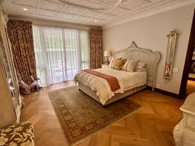 Spacious bedroom featuring elegant herringbone timber flooring, an ornate coffered ceiling, and large sliding glass doors providing natural light.