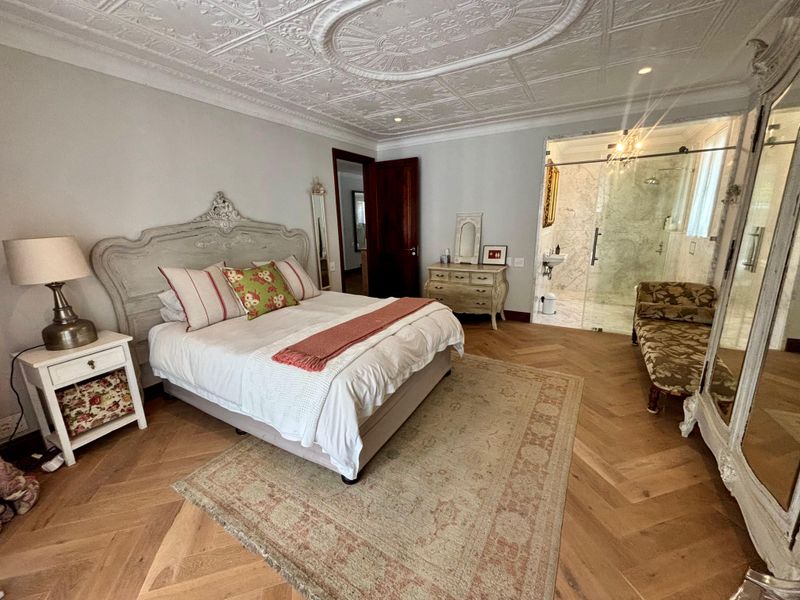 Spacious bedroom featuring elegant herringbone timber flooring, an ornate coffered ceiling, and an integrated glass-enclosed en-suite bathroom.