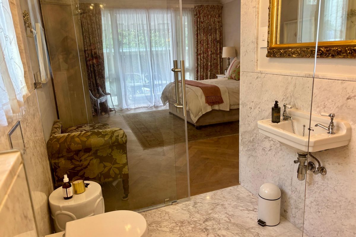 An elegant bedroom suite featuring a seamless transition to an en-suite bathroom with marble finishes, glass shower enclosure, and herringbone timber flooring.
