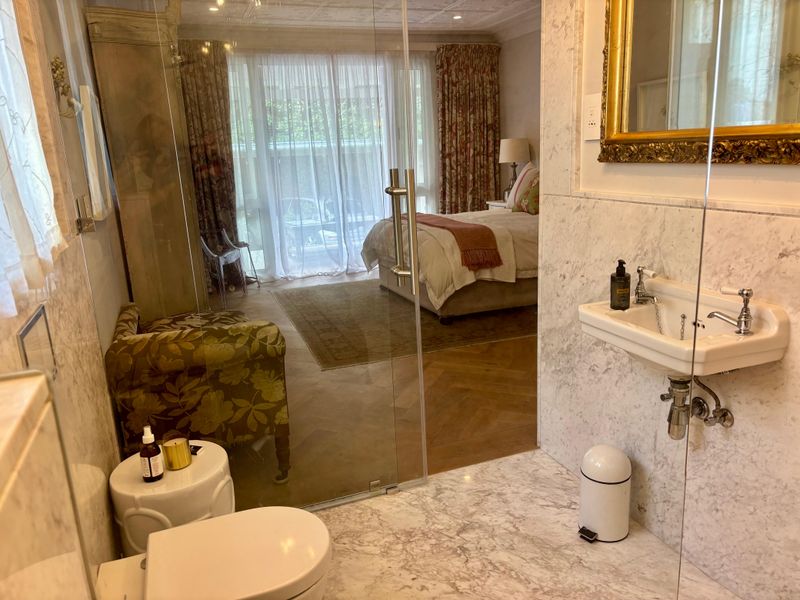 An elegant bedroom suite featuring a seamless transition to an en-suite bathroom with marble finishes, glass shower enclosure, and herringbone timber flooring.