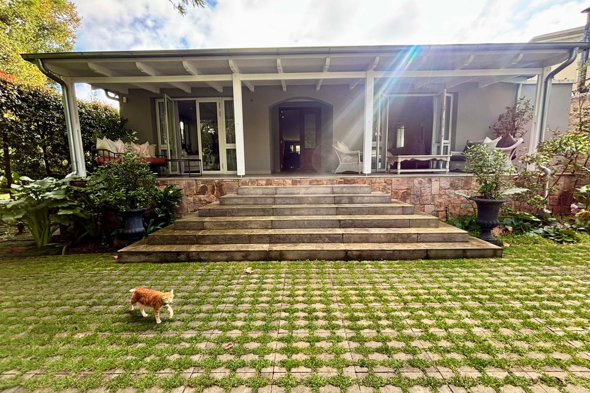 Rear view of the house featuring a covered patio with stone steps leading to a landscaped garden with grass pavers.
