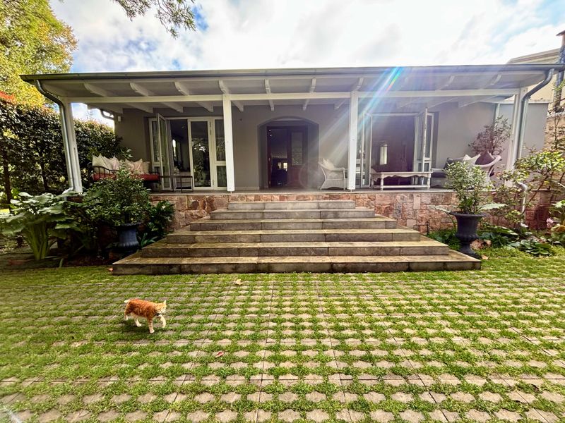 Rear view of the house featuring a covered patio with stone steps leading to a landscaped garden with grass pavers.