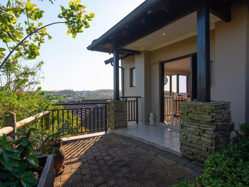 A covered patio featuring stone-clad pillars, tiled flooring, and a metal balustrade, offering elevated views of the surrounding landscape.