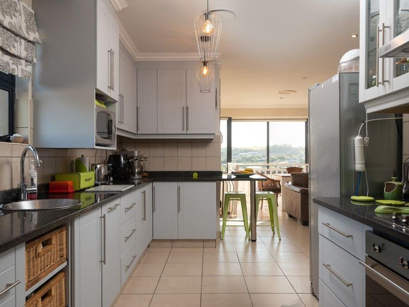 Modern kitchen featuring light grey cabinetry, granite countertops, built-in oven, and extractor fan, flowing into an open-plan living area with natural light.