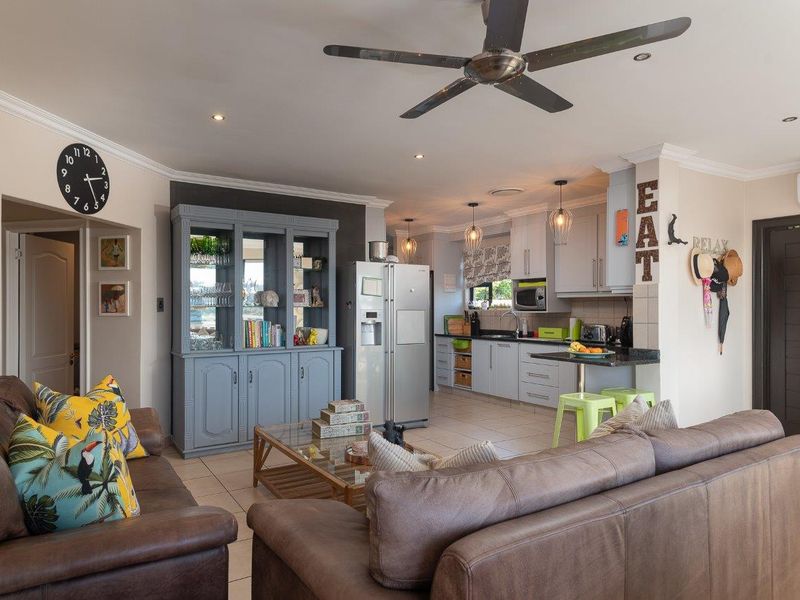 An open-plan living and kitchen area featuring tiled floors, recessed lighting, a ceiling fan, and a functional kitchen with granite countertops and built-in cabinetry.