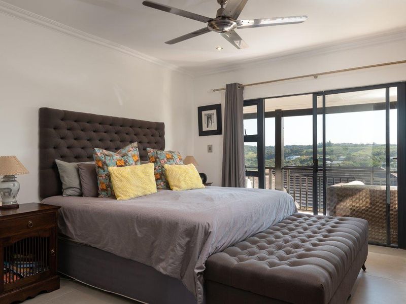 Spacious bedroom featuring tiled floors, a ceiling fan, and large sliding glass doors that open onto a private balcony with scenic views.