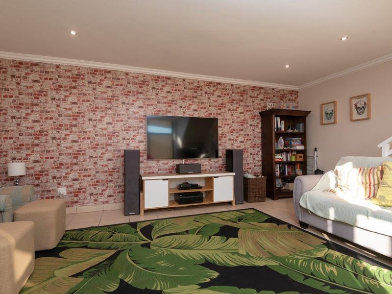 A comfortable living room featuring a brick-effect feature wall, tiled flooring, and recessed downlighting, creating a warm and inviting space.