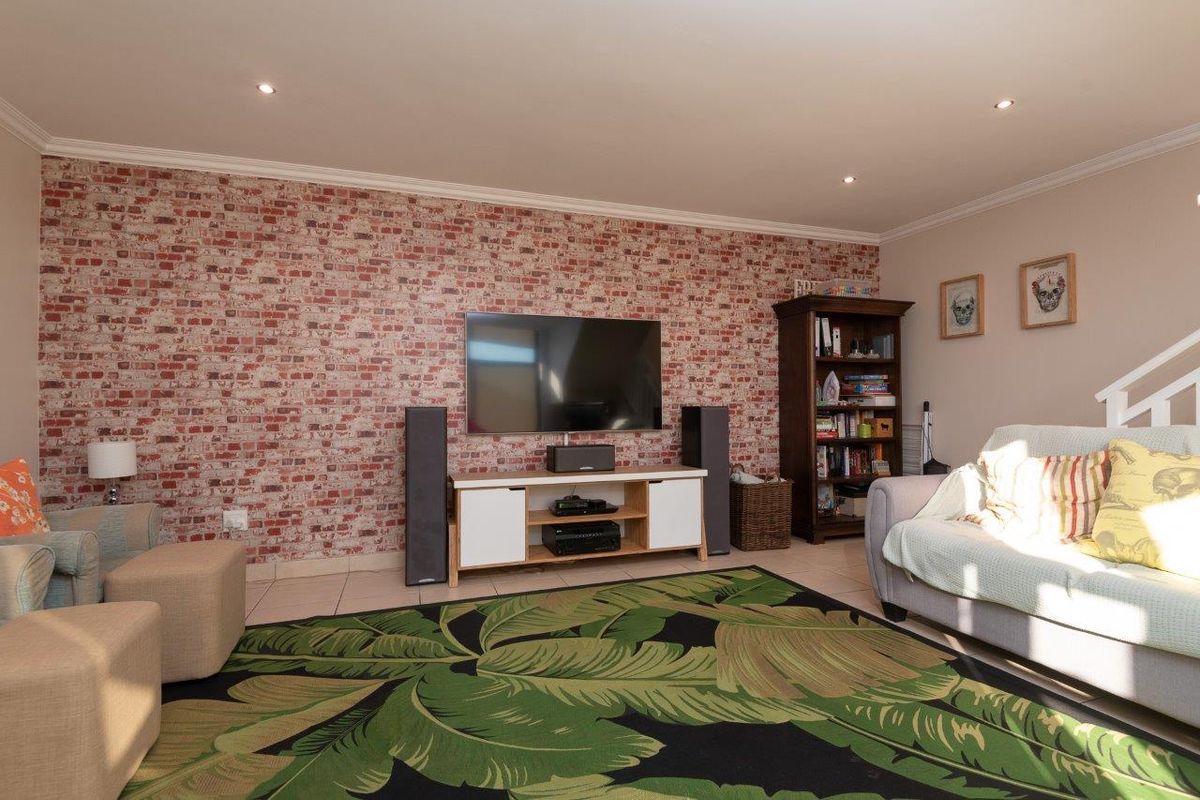 A comfortable living room featuring a brick-effect feature wall, tiled flooring, and recessed downlighting, creating a warm and inviting space.