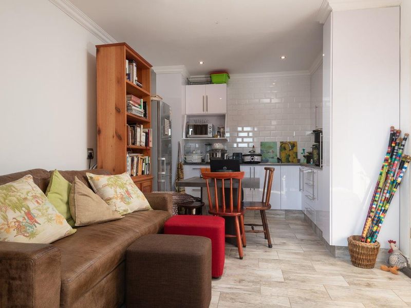 An open-plan living and kitchen area featuring white cabinetry, a subway tile backsplash, and tiled flooring with crown molding details.