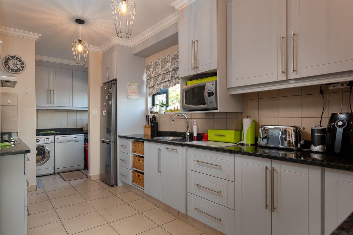 A well-maintained kitchen featuring light grey cabinetry, granite countertops, tiled backsplash, and a functional layout with an adjacent laundry area.
