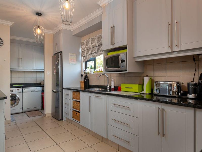 A well-maintained kitchen featuring light grey cabinetry, granite countertops, tiled backsplash, and a functional layout with an adjacent laundry area.