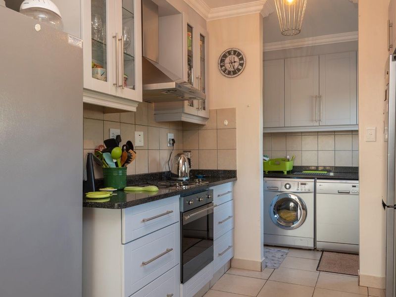 A well-maintained kitchen featuring light-toned cabinetry, granite countertops, built-in oven, gas hob, and an adjoining scullery area with laundry facilities.