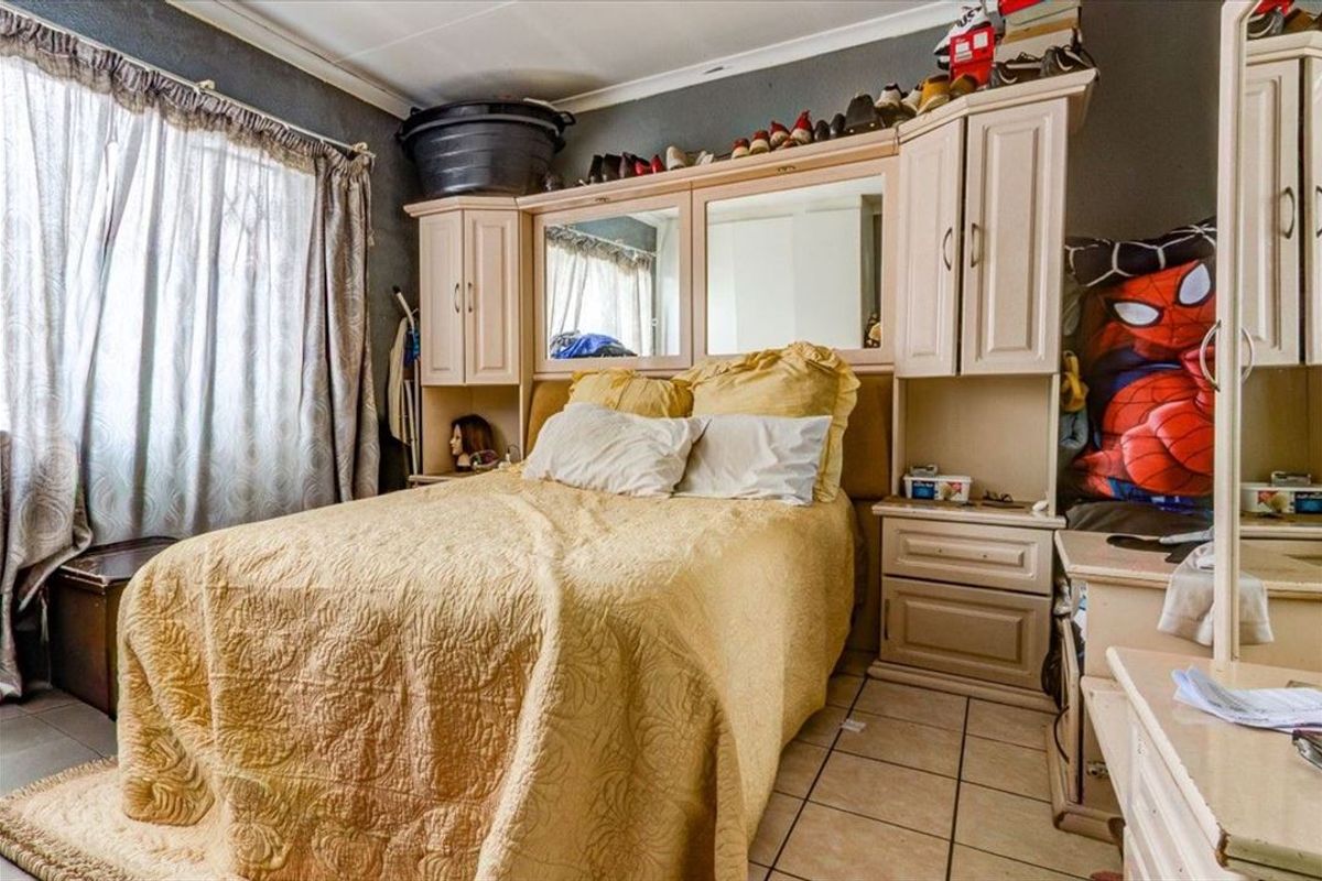 A bedroom featuring built-in cupboards and tiled flooring, offering a functional space that could benefit from cosmetic updates and modern finishes.
