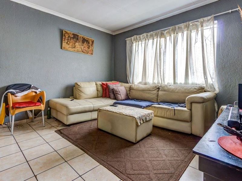 A living room featuring tiled flooring, coved ceilings, and a window fitted with security bars.