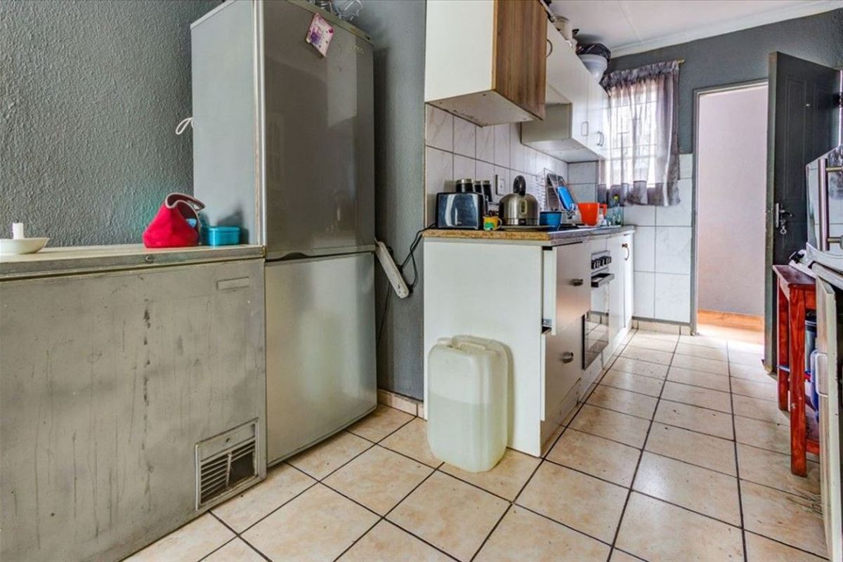 A compact kitchen featuring tiled flooring, built-in cabinetry, and a tiled backsplash, offering a functional layout in need of cosmetic updates.