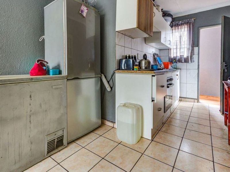 A compact kitchen featuring tiled flooring, built-in cabinetry, and a tiled backsplash, offering a functional layout in need of cosmetic updates.