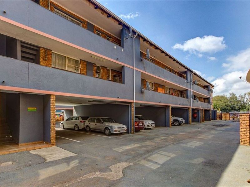 Exterior view of a multi-story apartment complex featuring covered ground-level parking bays and private balconies for each unit.