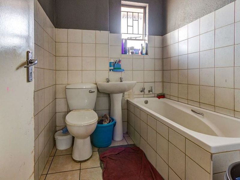 A compact bathroom featuring a standard bathtub, pedestal basin, and toilet with tiled walls and flooring, requiring cosmetic updates to improve its condition.