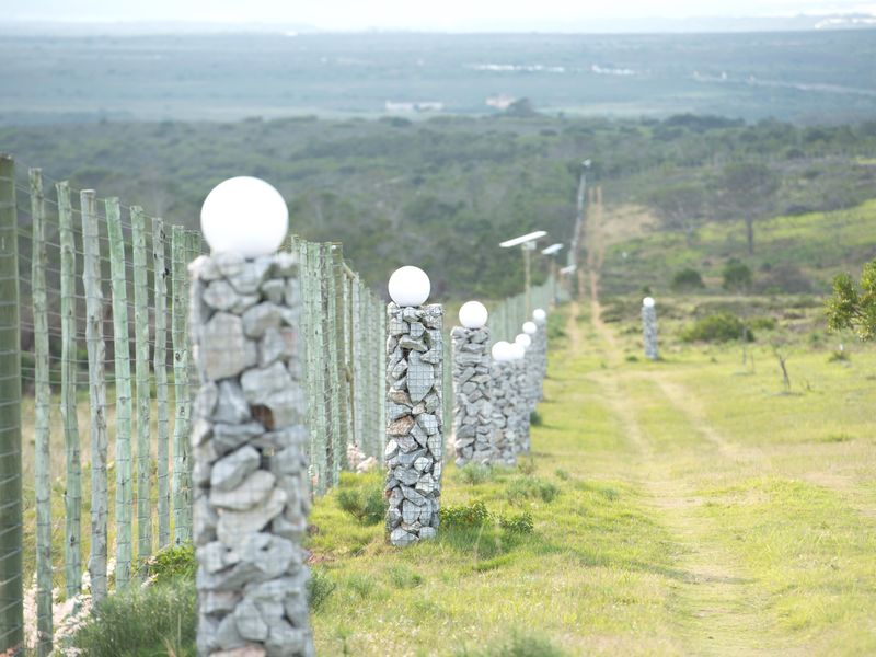 A well-maintained perimeter boundary featuring gabion stone pillars with integrated solar lighting and electric fencing, overlooking a vast natural landscape.