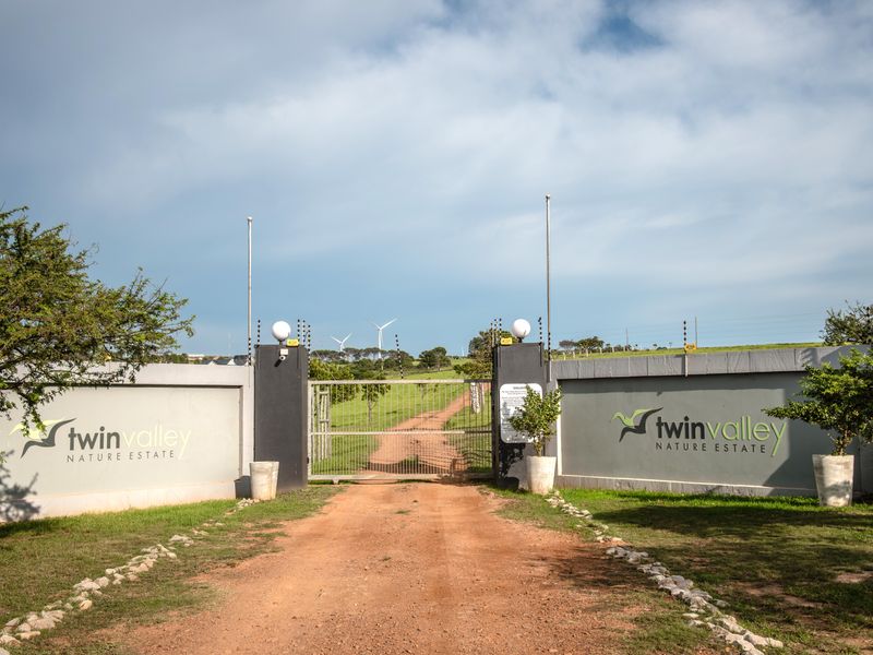The main entrance gate to Twin Valley Nature Estate, featuring a secure perimeter wall, electric fencing, and a dirt access road.